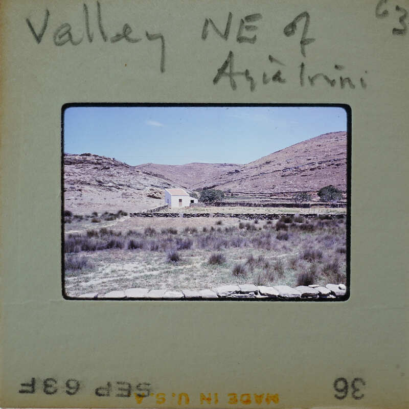 A vintage photo of a rural landscape with mountains and a small white building.