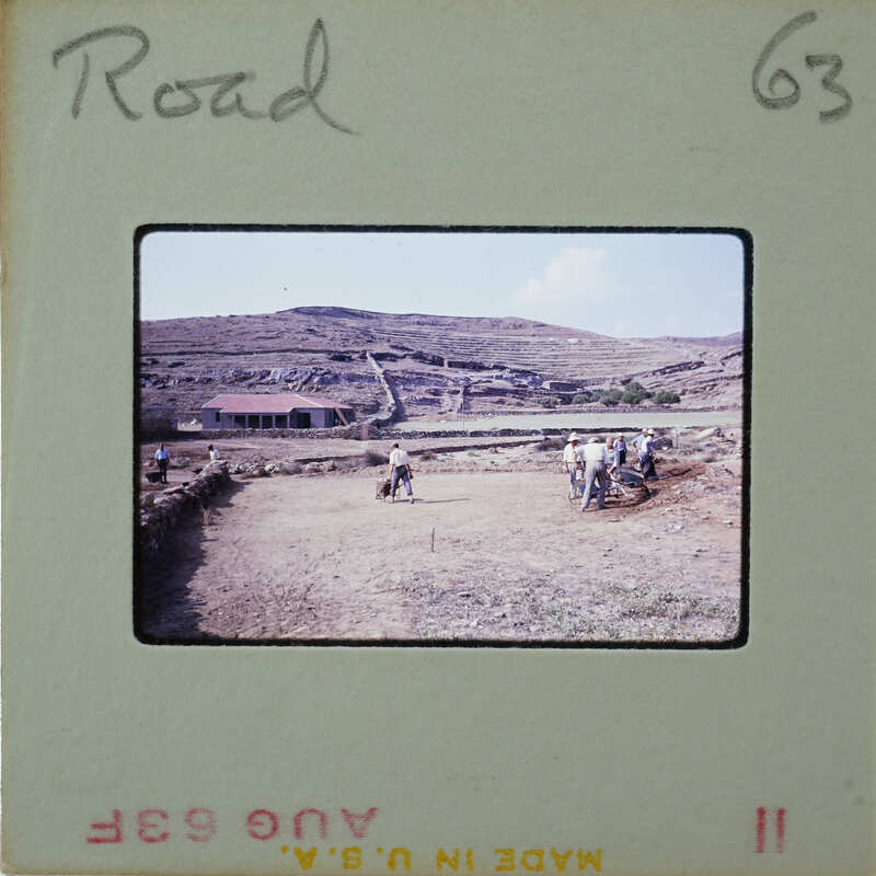 A group of people working on a dirt road with mountains in the background.