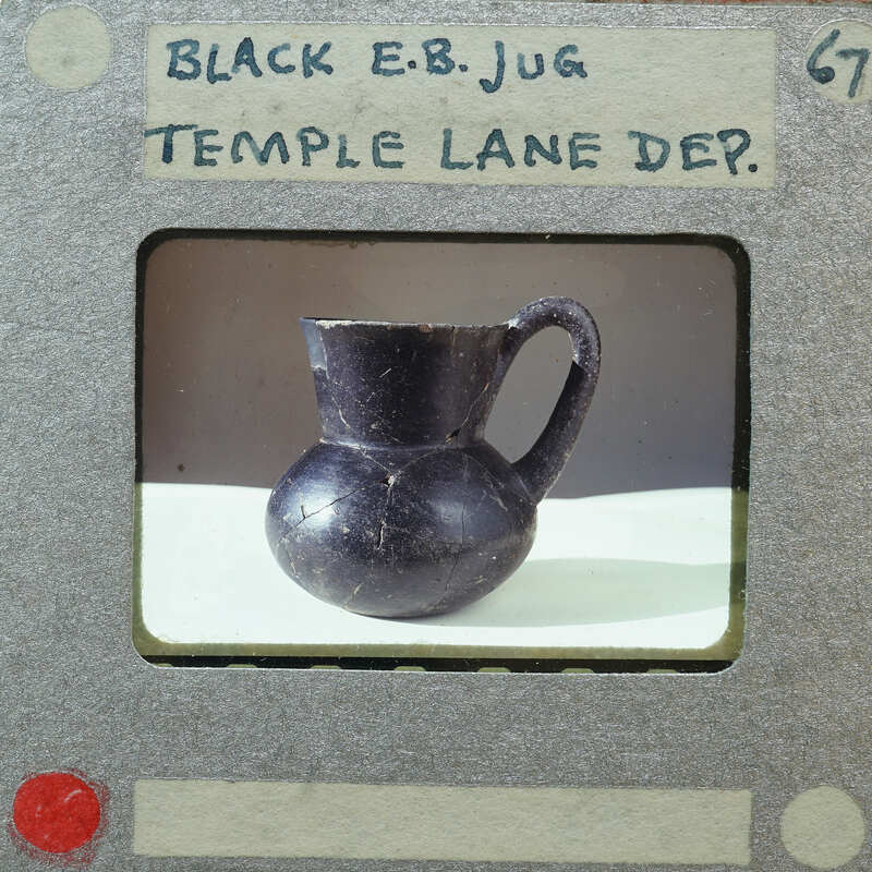 A black jug with a handle and spout, displayed on a white surface within an image frame.