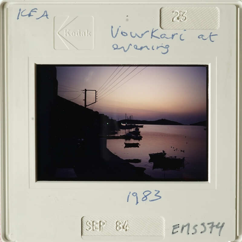 Sunset over calm water with boats and distant hills.