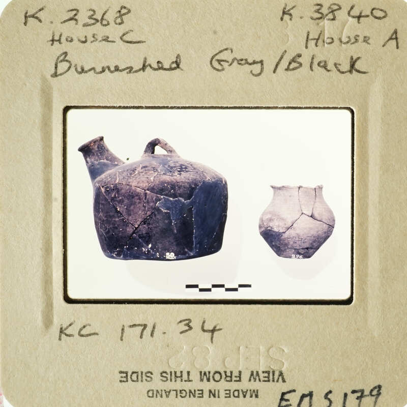 Two ancient vases, one intact and one broken, displayed on a white surface with labels.