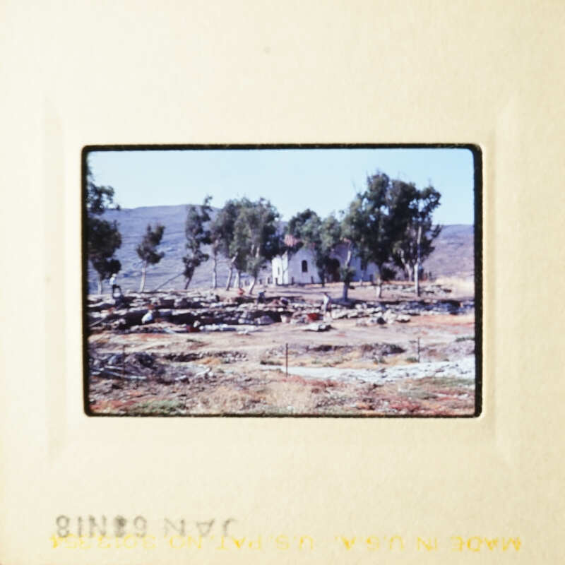 A vintage photo of an arid landscape with a few trees and a church, taken during the day under clear skies.