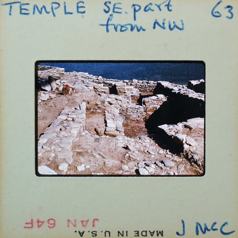 Detail of Temple stone walls with doorway, in slanting light with water in background.