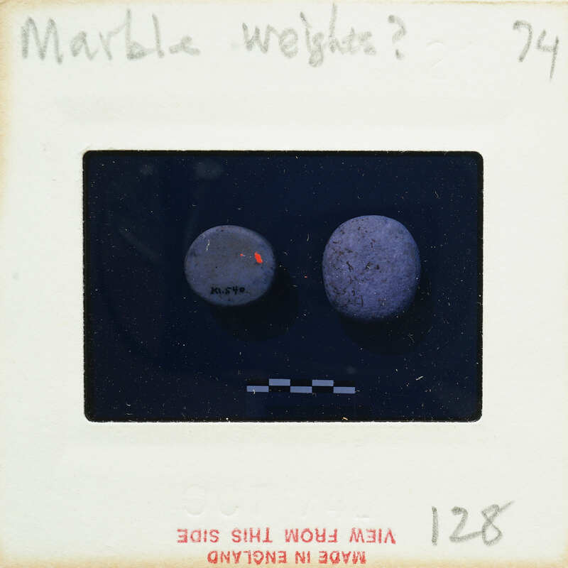 The image is a photograph of two marble weights on a scale, with the focus being on the right weight which appears to be heavier or denser than the left one.