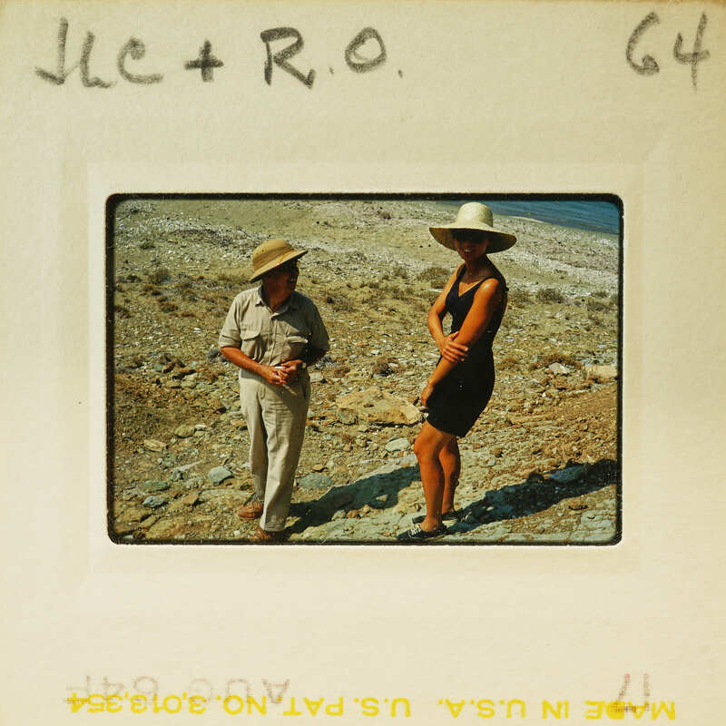 Man and woman standing on rocky terrain with ocean in background.