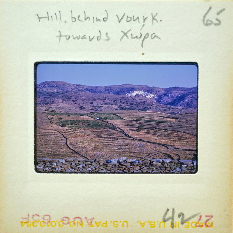 A vintage photograph of a mountainous landscape with terraced fields and a village below.