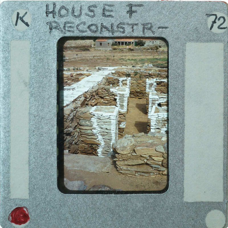 A photograph of an archaeological site with stone ruins, placed within a film negative holder with handwritten labels.
