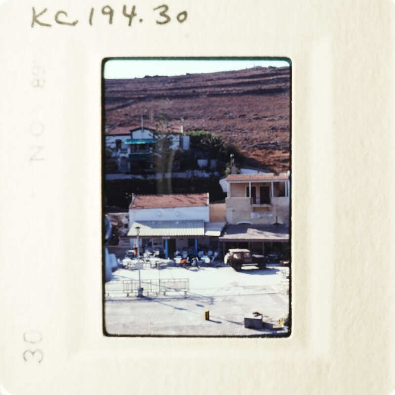 Photo depicts a rural village scene with buildings and vehicles, taken from an elevated perspective.