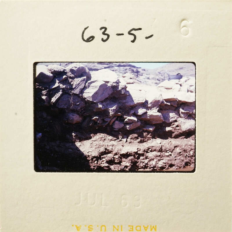 Stone wall with dirt and rocks on ground.