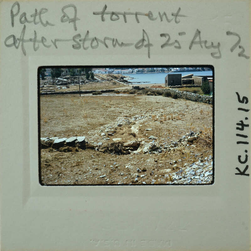 A photograph of a barren landscape with stone walls and a body of water, possibly the sea, in the background.