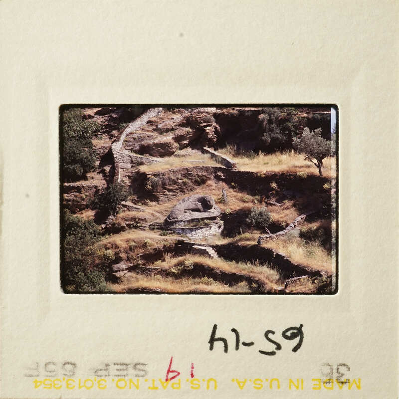 A photograph of a rocky landscape with shrubs and trees, featuring an old slide mount with handwritten notes.