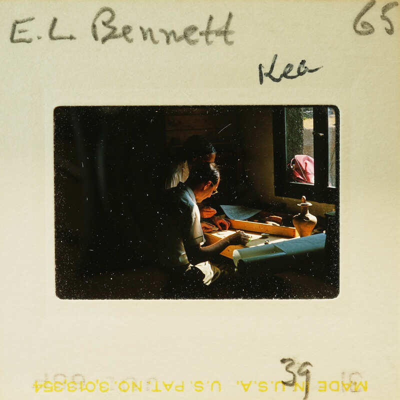 Two people working studying artifacts at a table with natural light coming through a window.