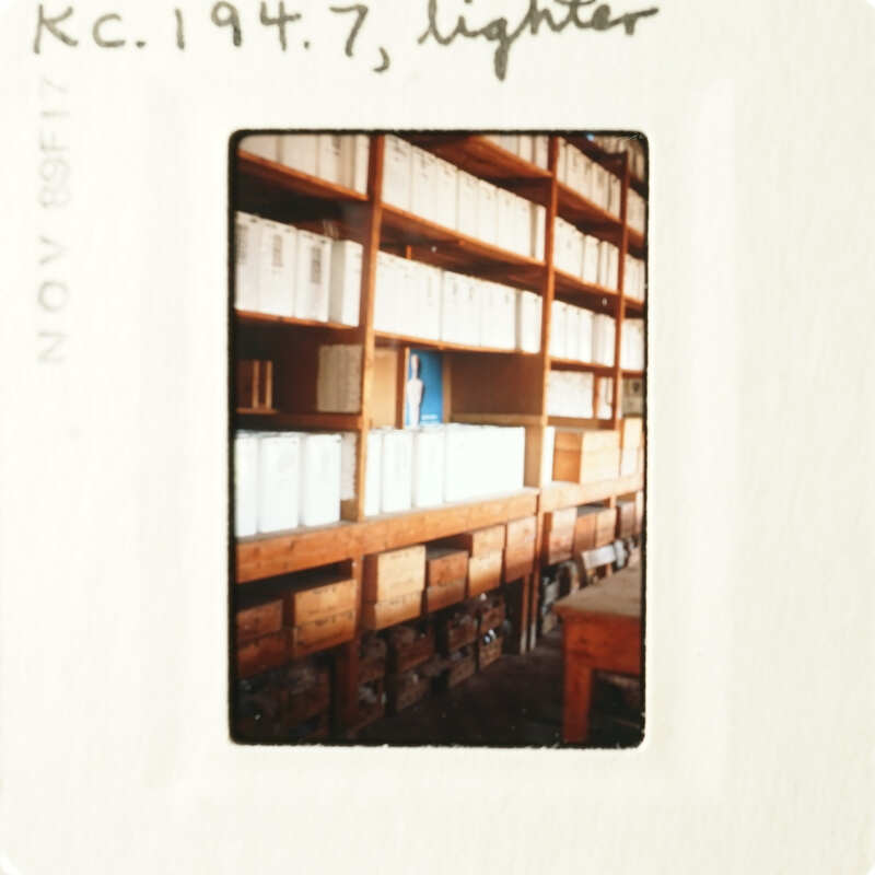 A postcard with an image of a room filled with shelves of books and papers, taken from a low angle.