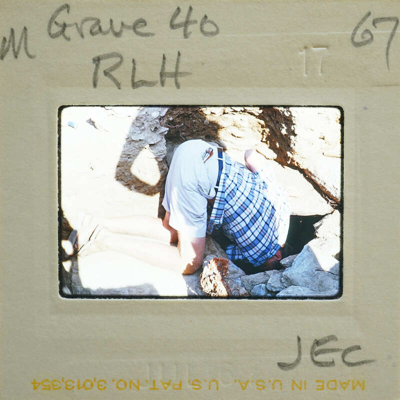 A man bent over, working on a rock or digging with a pickaxe.