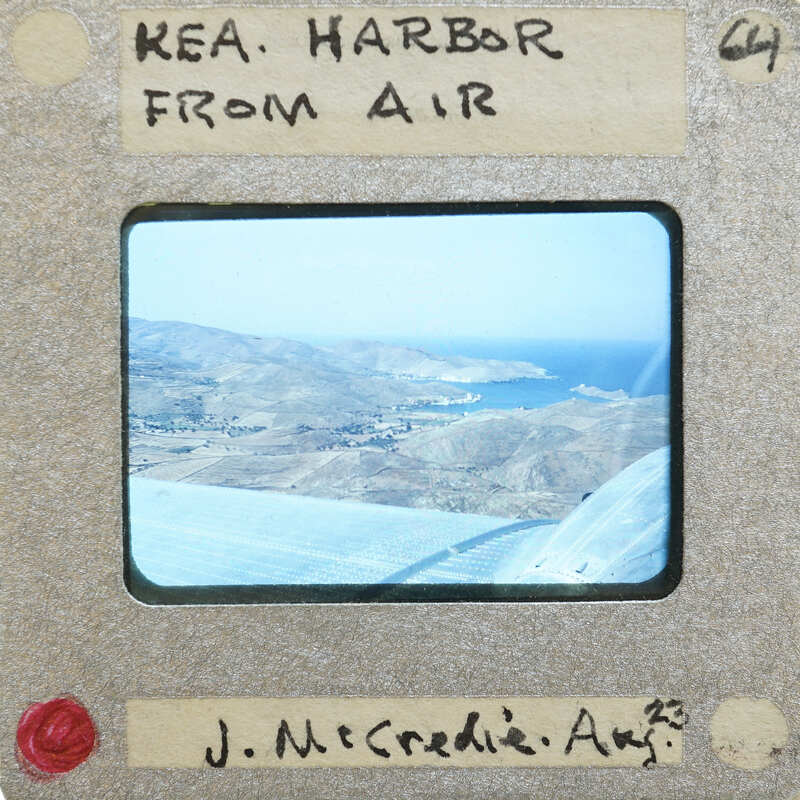 Aerial photograph of a harbor with mountains and water, taken from an airplane window.