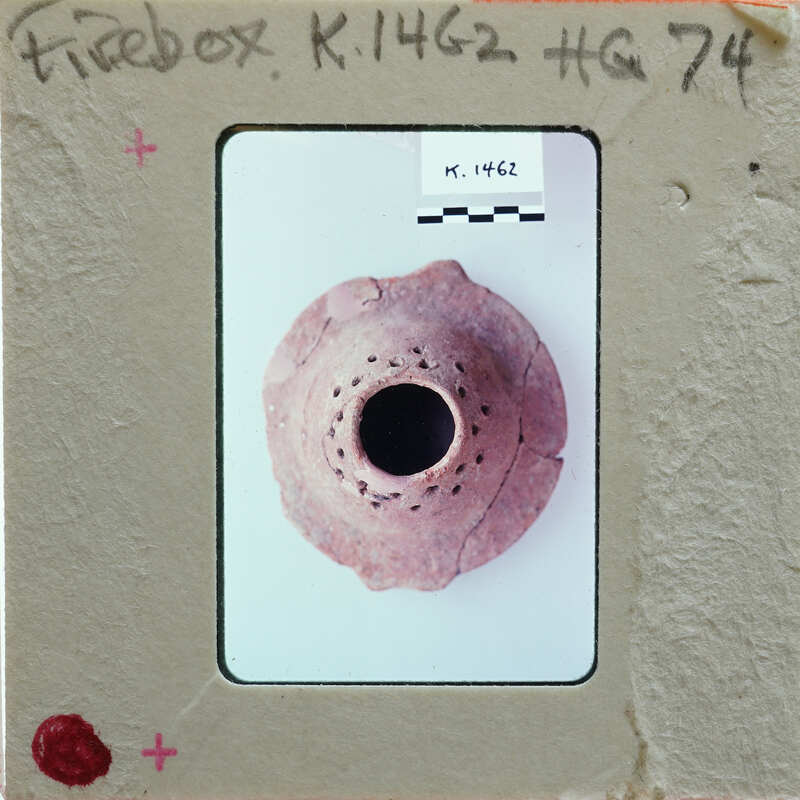 A small, round clay object (K.1462) with a hole in the center and multiple holes around its circumference.