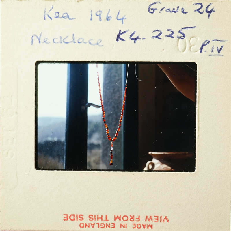 A photograph of an antique necklace with red beads and a gold clasp, displayed against a window view.