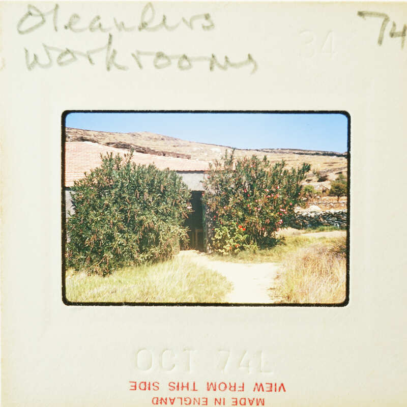 A vintage photograph of a rustic building with trees and shrubbery, labeled "CLEANERS WORKSHOPS" on the front.