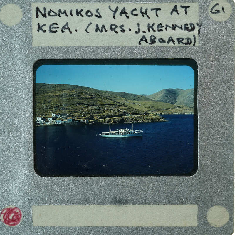 Photo of a boat on water with mountains in the background, labeled "Nomikos Yacht at Kea / Mrs. J. Kennedy Aboard".