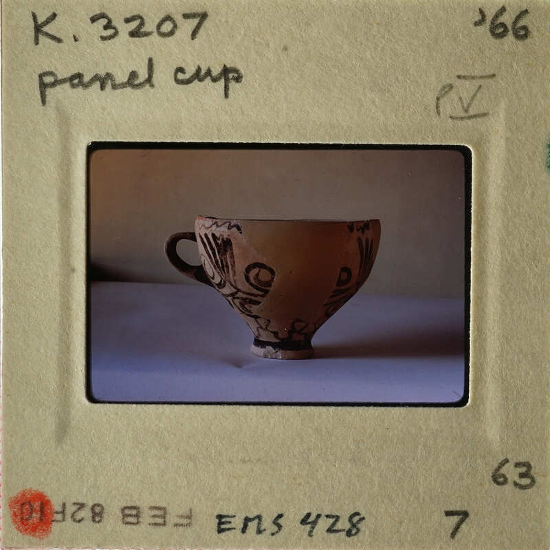 A beige ceramic cup with intricate designs, photographed on a white surface.