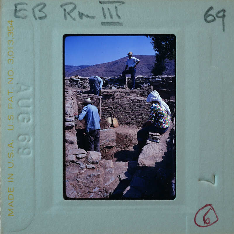 Archaeologists excavating a site with stone ruins and dirt mounds.