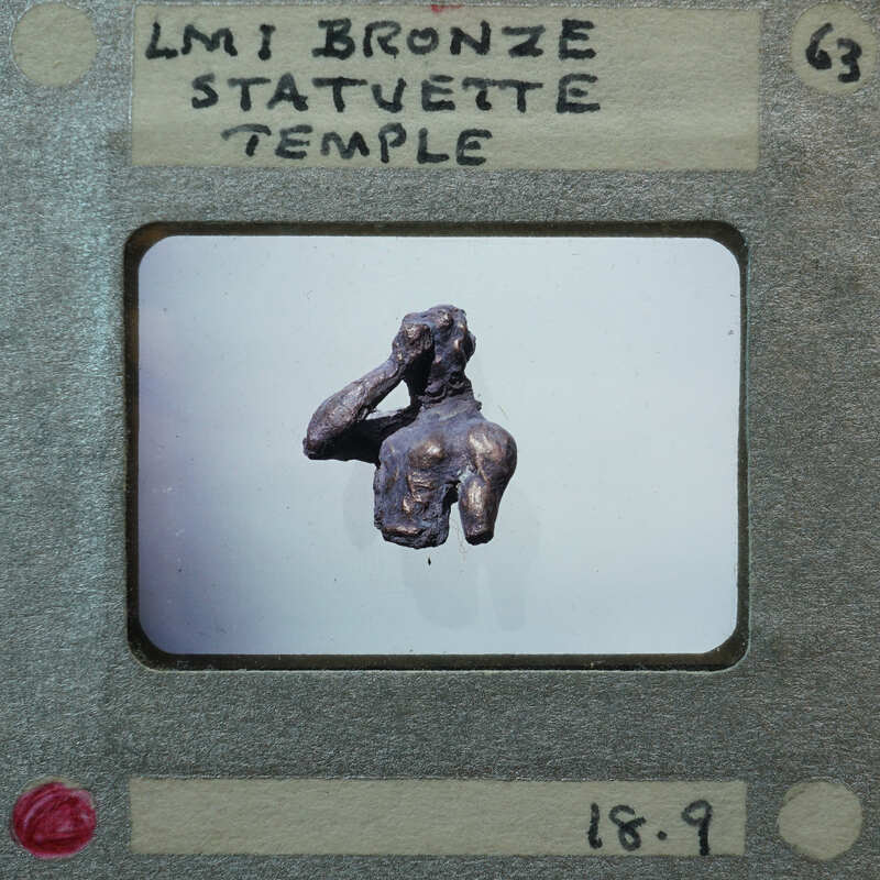 Small bronze statue of a figure with hands raised, displayed on a white surface.