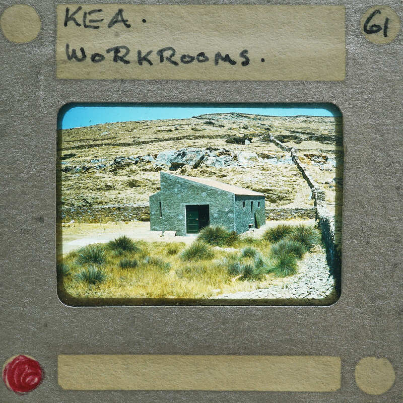 A photograph of a small stone building with mountains in the background, presented on a faux film strip.