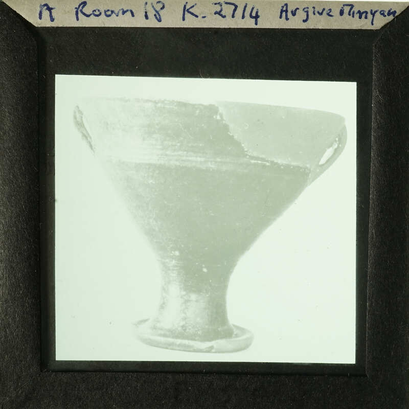 A black and white photograph of an ancient Greek drinking cup with visible cracks.