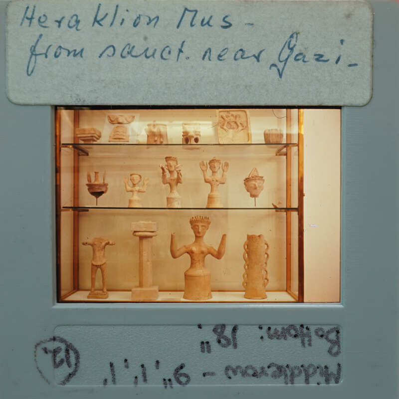 Ancient figurines displayed on shelves inside a case, with labels indicating their origin.