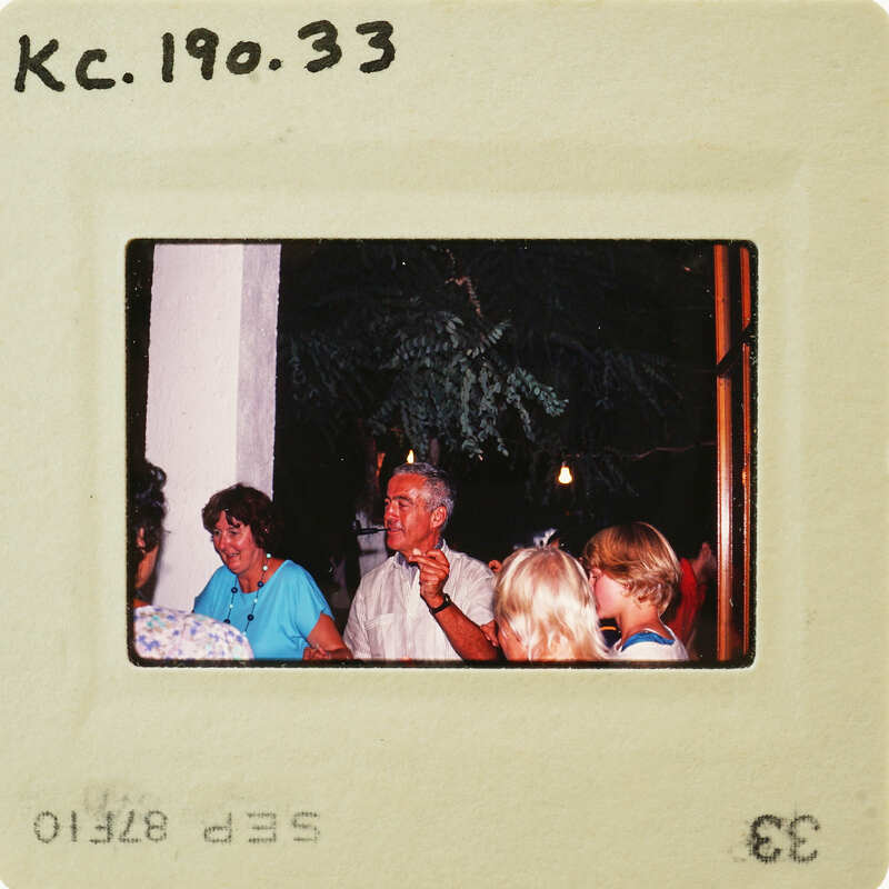 The image is a photograph of an older man and woman standing outside at night, with trees behind them. Catalog number KC.190.33