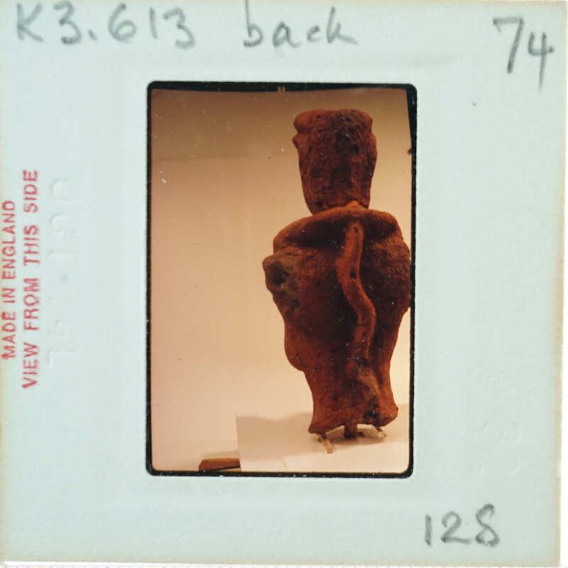 Clay figurine from behind, displayed with a white background and a label.
