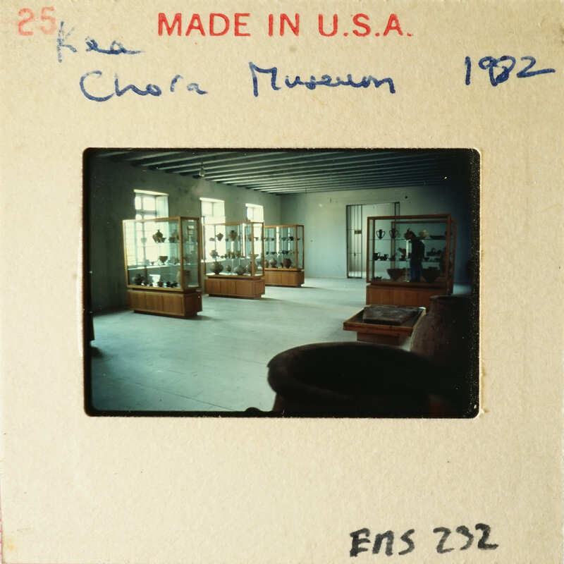 Museum display case with glass cabinets and wooden bases, housing various items on shelves.