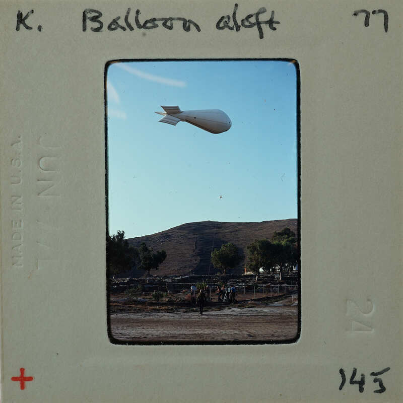 A large white balloon floating above a landscape with mountains and trees.