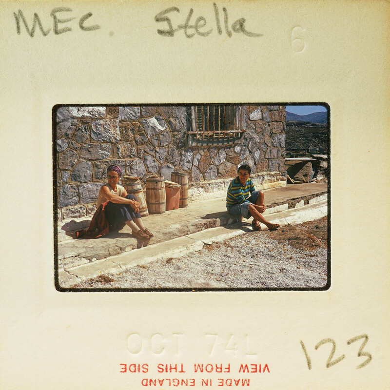 Two people sitting on a ledge with stone building behind them, captured on an old photograph.