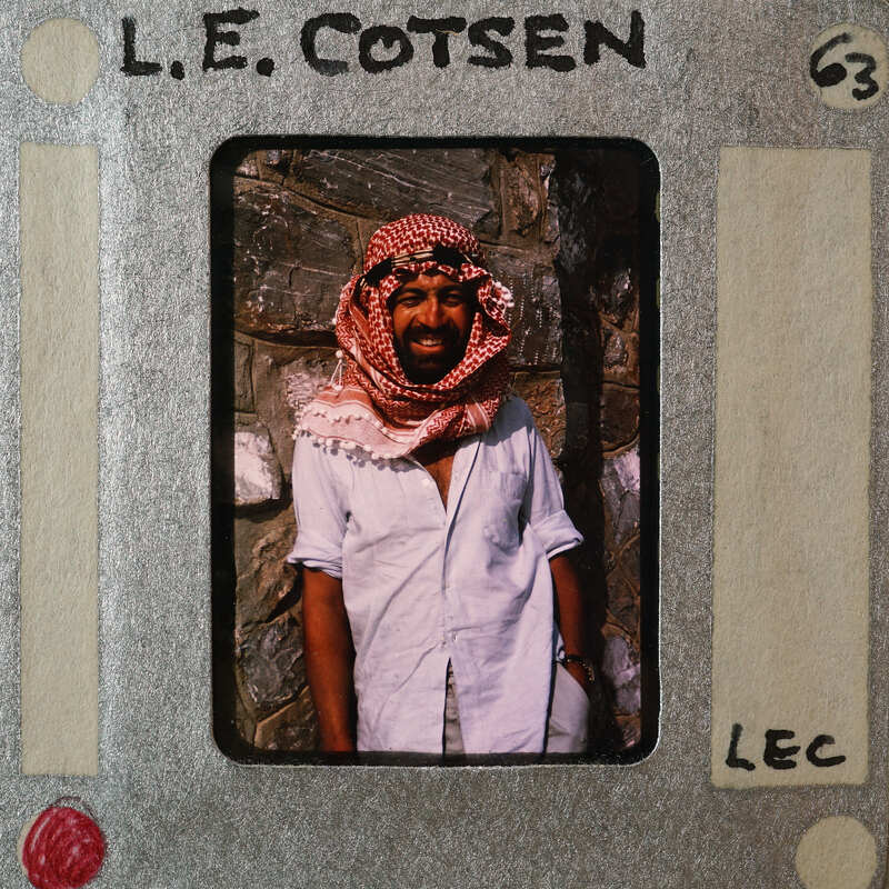 A man wearing a headscarf and standing in front of a stone wall.