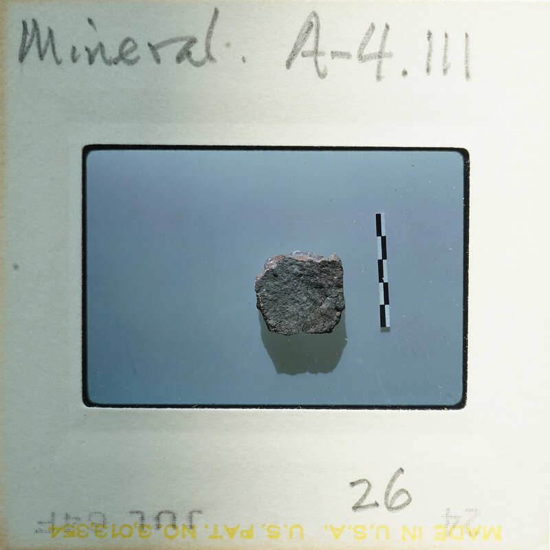 A small, dark rock on a light surface with a label and number.