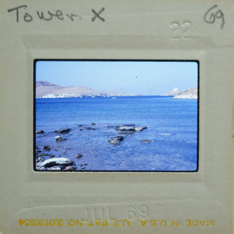 Picture of a serene beach with calm waters and distant mountains, taken on film.