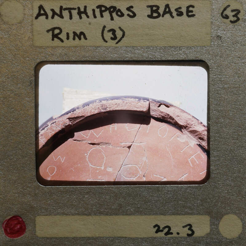 Old photograph of an ancient artifact with visible cracks and writing on it, displayed on a film strip.