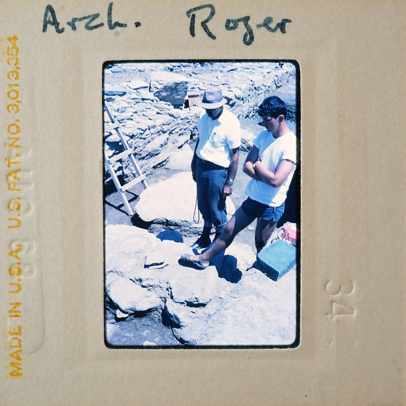 Two men standing near rocks with a vintage Polaroid photo border.