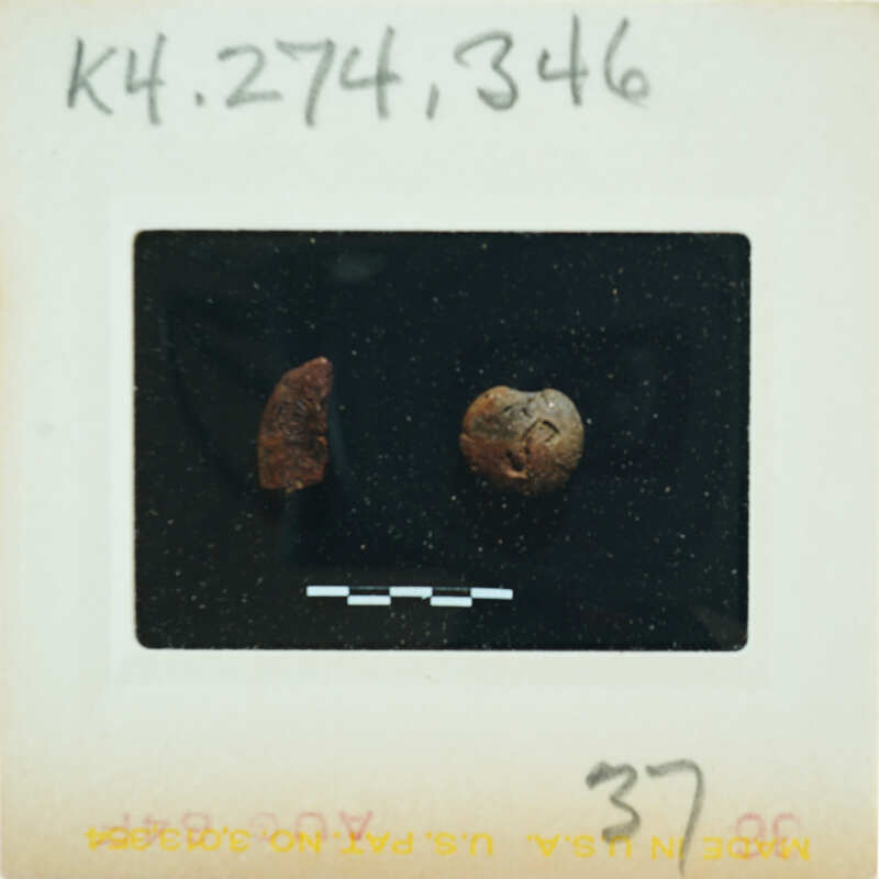 A photograph of a small, round object with markings on it, possibly an artifact or a coin, placed against a dark background.