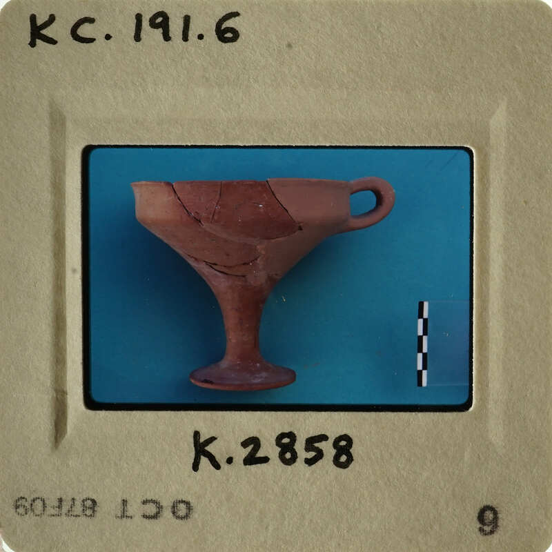 Ancient clay cup with handle on blue background, photographed and labeled.