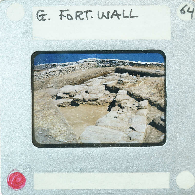 Picture of a stone wall with grass on top, taken from a distance and framed within an old photograph border.