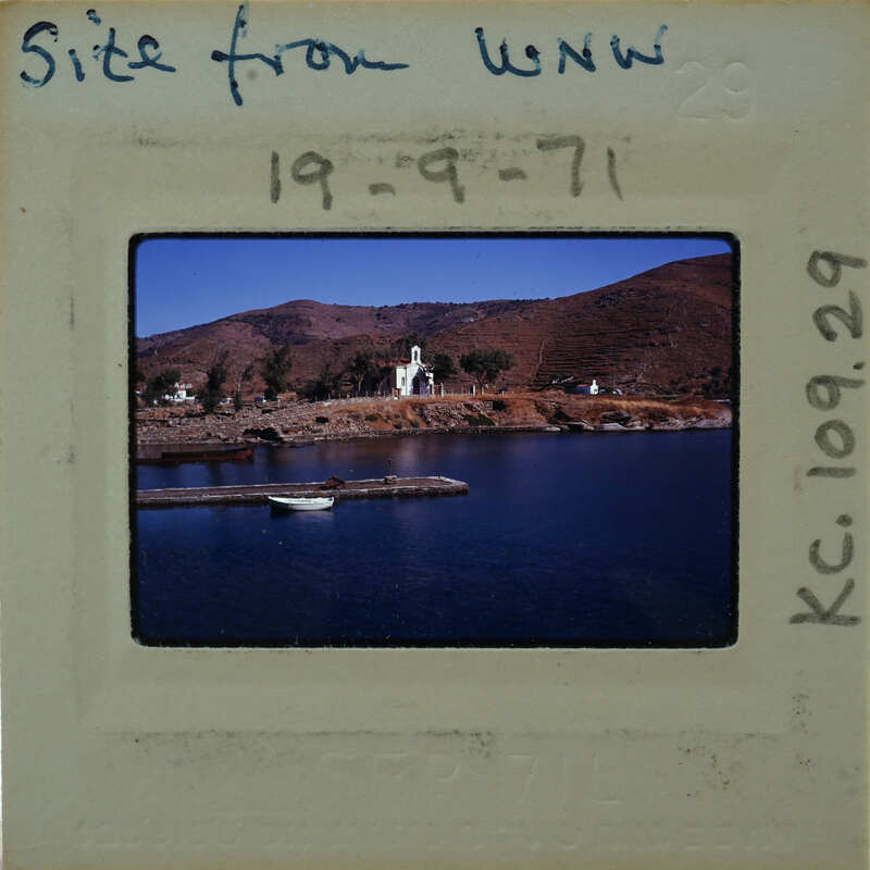 A vintage photograph of a coastal landscape with mountains and water, featuring a pier and boat.