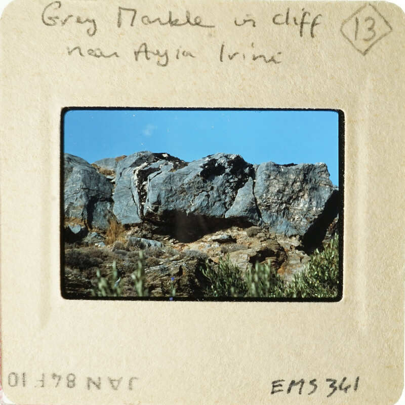 Rocky cliff with vegetation under a blue sky.
