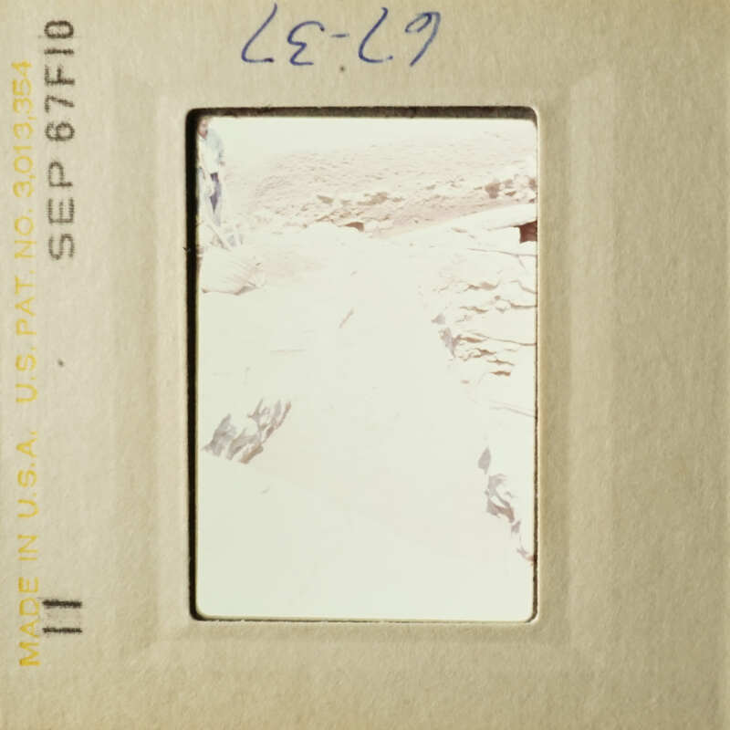 A blurry photograph of an outdoor scene, possibly taken with a telephoto lens, showing a path leading into a rocky landscape.