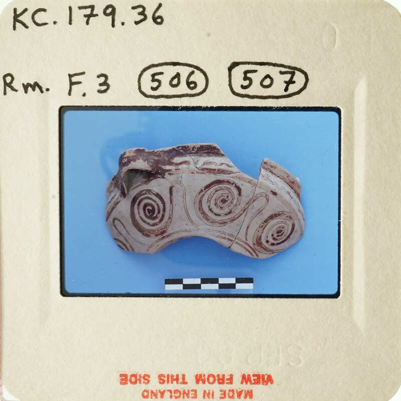 Ancient artifact with spiral designs on a blue background, photographed and labeled for documentation.