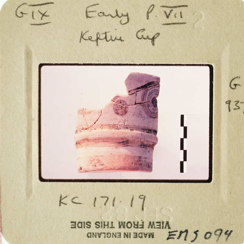 A fragment of an ancient artifact, possibly pottery with visible cracks and textures, displayed against a white background.