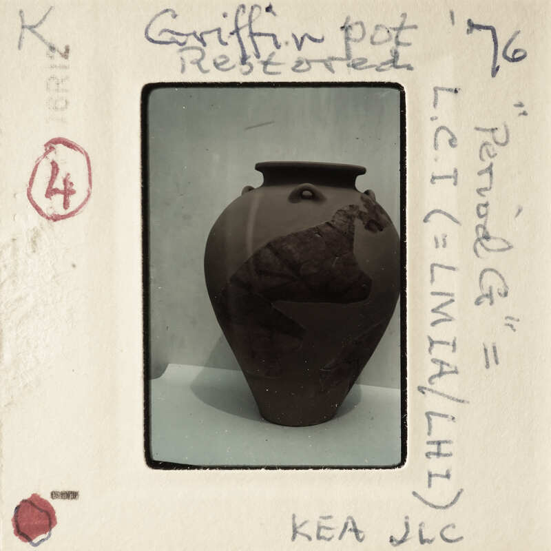 A photograph of a brown vase with markings, displayed on a white surface.
