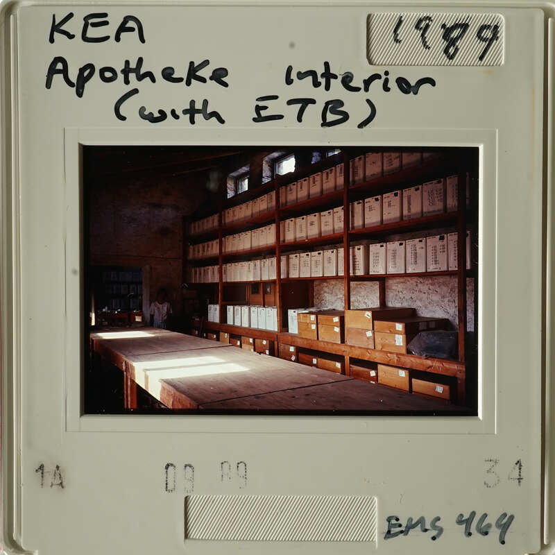 Old photograph of an interior room with shelves filled with boxes and a table in front.