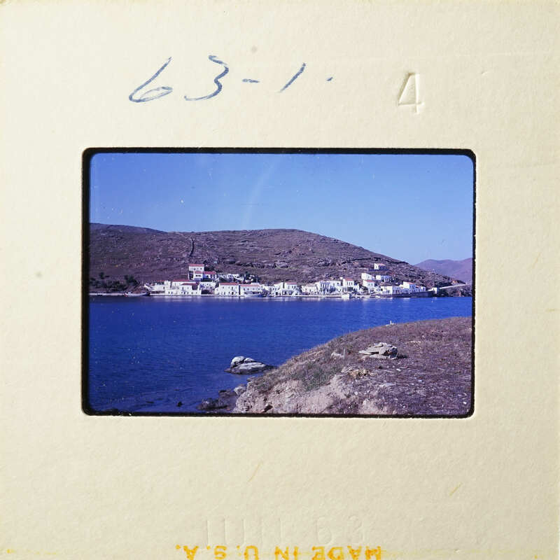 A coastal village with houses and boats on calm waters, under a clear sky.